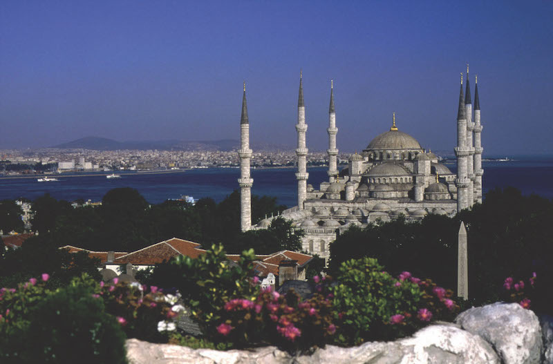 View of Hagia Sophia and Bosphorus Strait in the background. Hagia Sophia has 6 tall spires surrounding a large structure with dome on top.