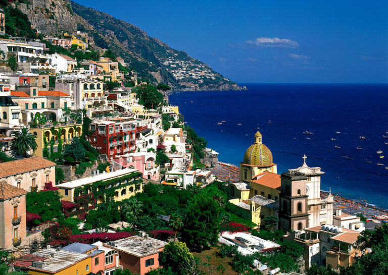 Positano, Amalfi Coast, Campania, Italy Cliffside town with several buildings along the slope, all with a view of the ocean. There are many sailboats and boats on the water.