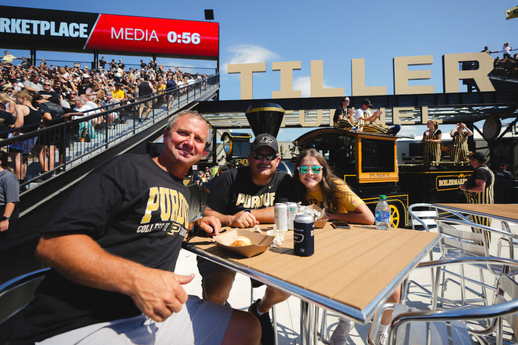 2 men and a girl sitting at the Tiller Tunnel patio at a Purdue Football game