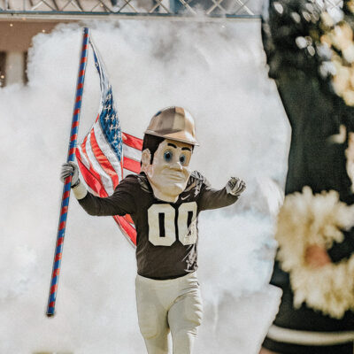 purdue pete running onto the football field waving an american flag