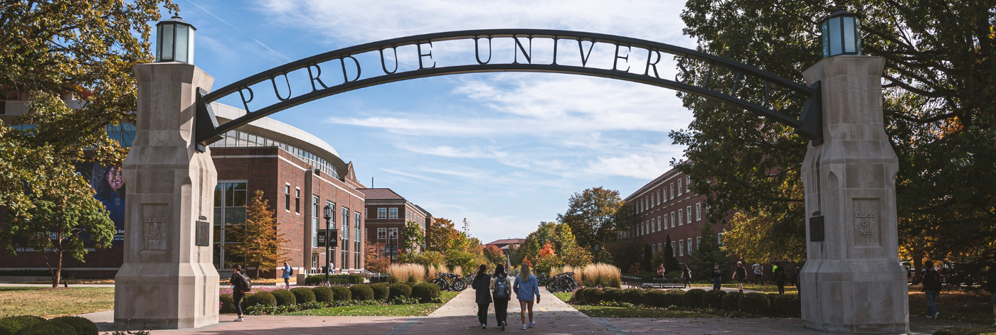 Image featuring Purdue University entrance with three student walking on campus.