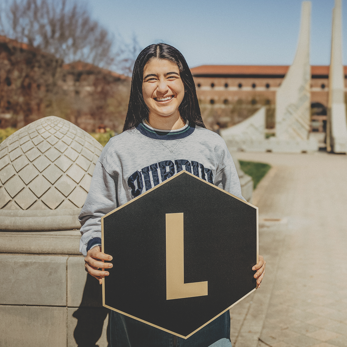 Student holding a "L" hexagon sign