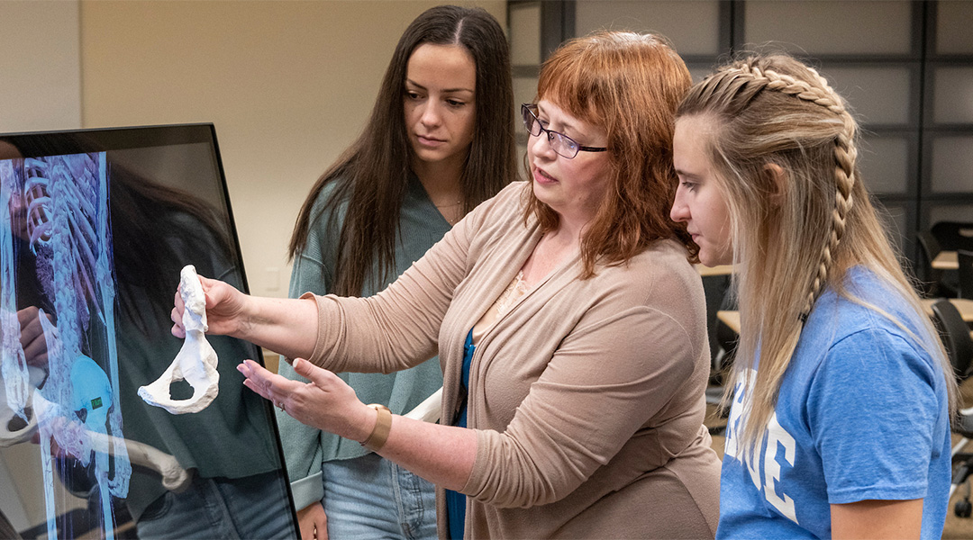 Three women looks at a human bone together