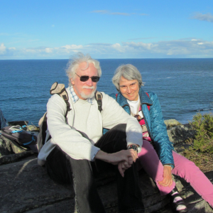 A man and a woman sitting in front of a body of water smiling at the camera