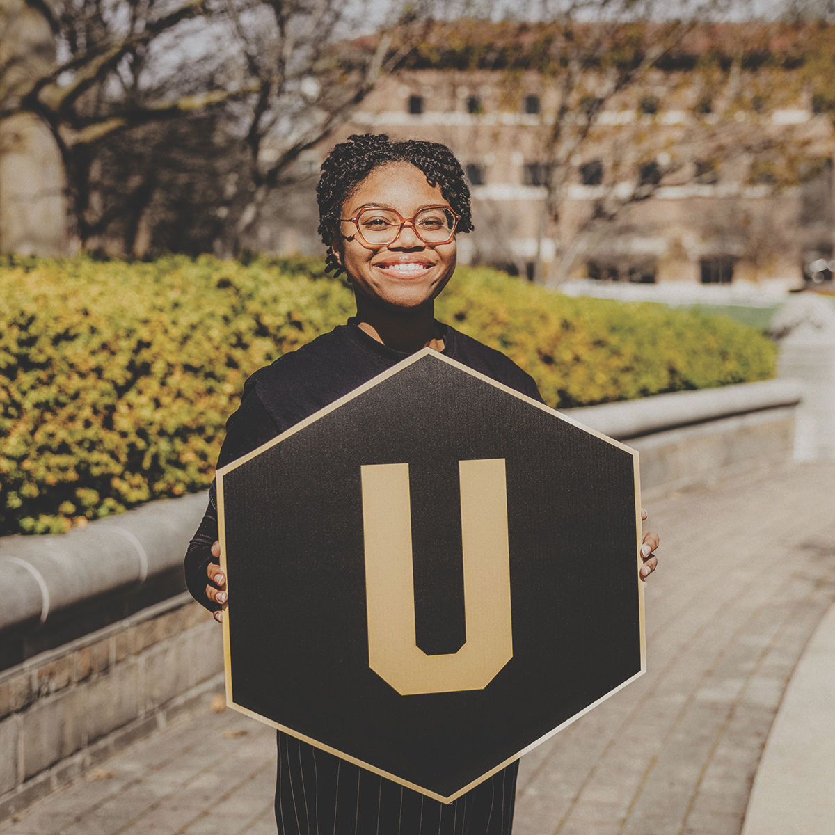 Student holding a "U" hexagon sign