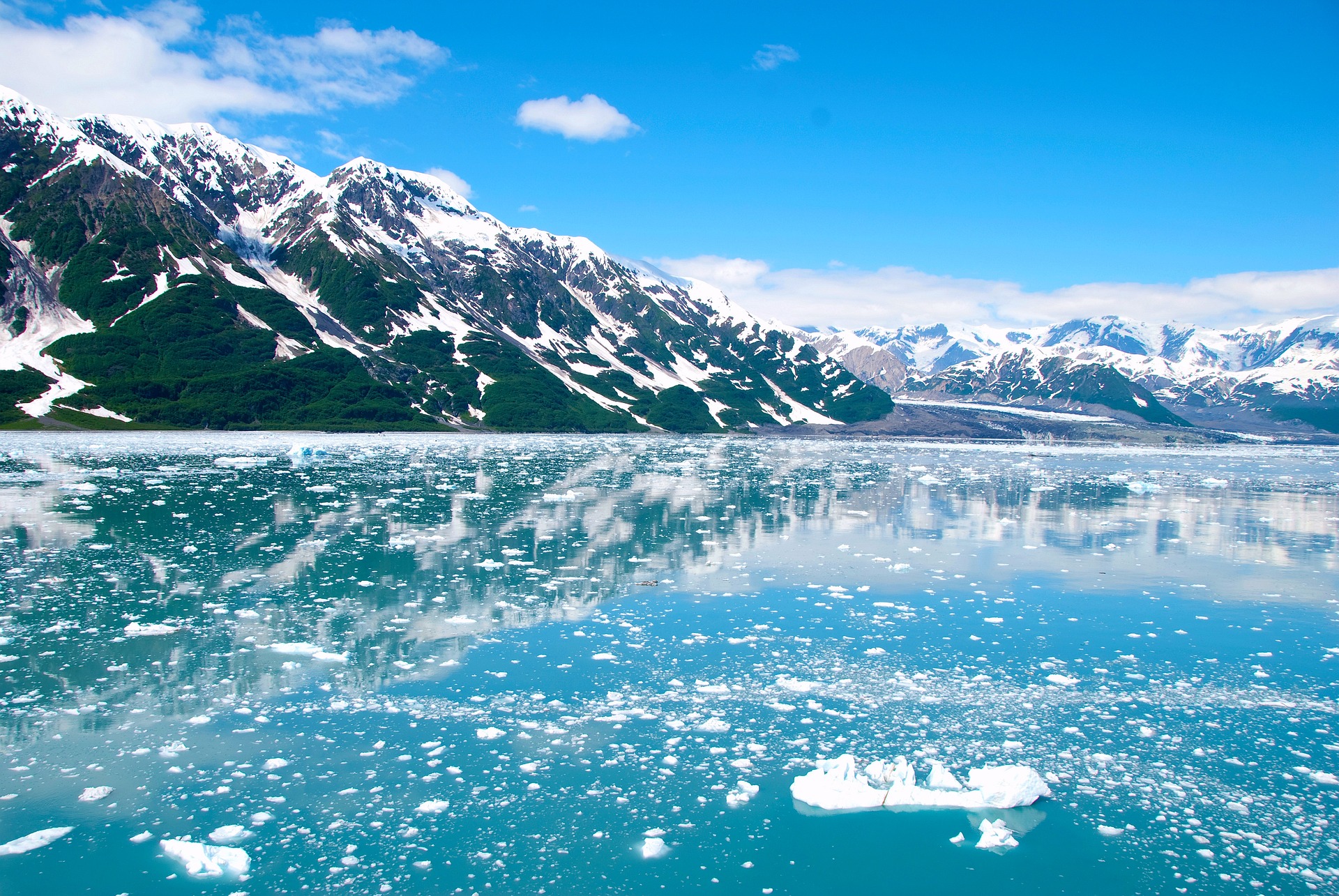 Image featuring Alaska's mountainous landscape with water reflection and a blue sky.