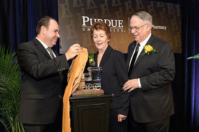 An image showing Purdue College of Pharmacy Dean Eric Barker, left, presents JeanAnne and James Chaney with the crystal Boilermaker Special in 2018. (Purdue University photo/John Underwood)