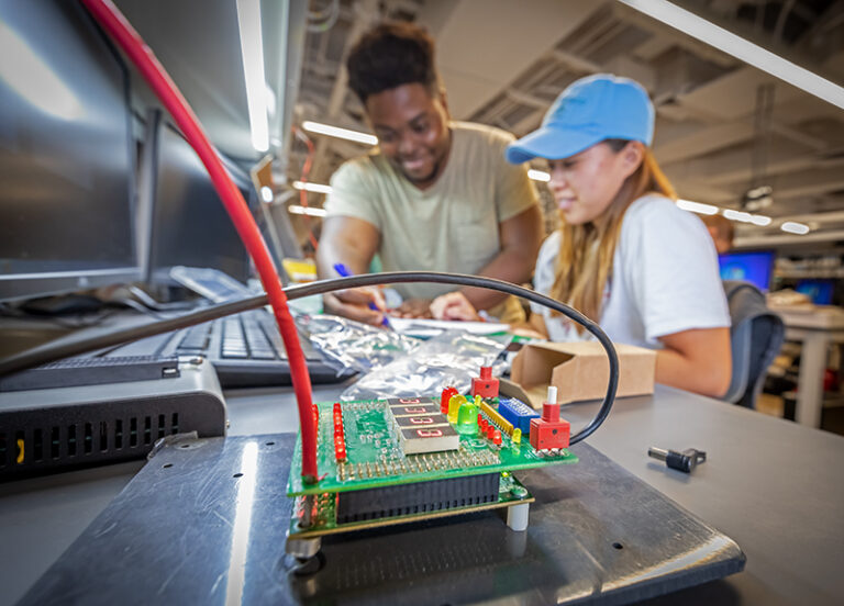 A young man and woman in a lab sitting in front of monitors doing lab work together