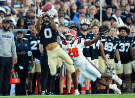 The image shows a Purdue University football player leaping through the air to catch the ball.