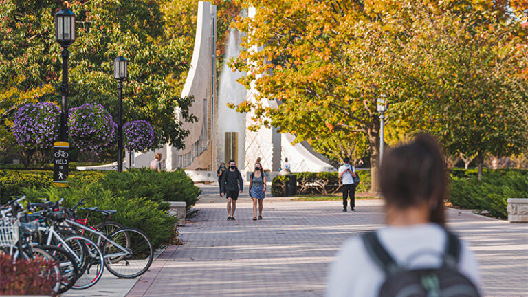 View of Engineering Mall with trees in fall color. There are a few students with backpacks walking.