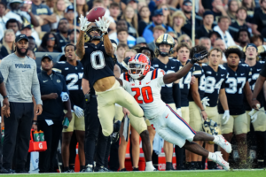 The image shows a Purdue University football player leaping through the air to catch the ball.