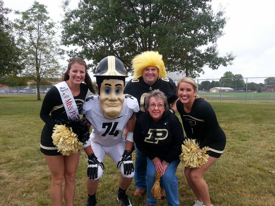 A man and a woman posing for a picture with 2 Purdue cheerleaders and Purdue Pete