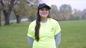 Naomi Matley - wearing yellow shirt and standing in front of trees.